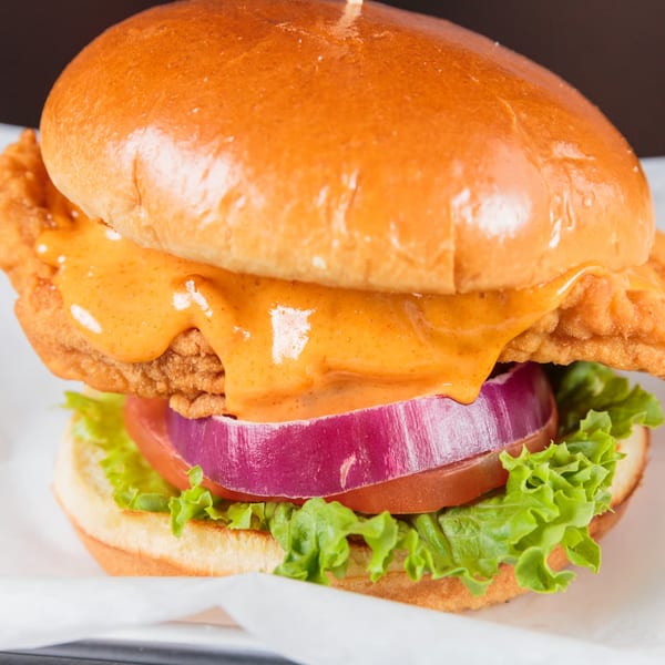 A crispy chicken sandwich from The Burger Life, with sauce, red onion, tomato, and lettuce.