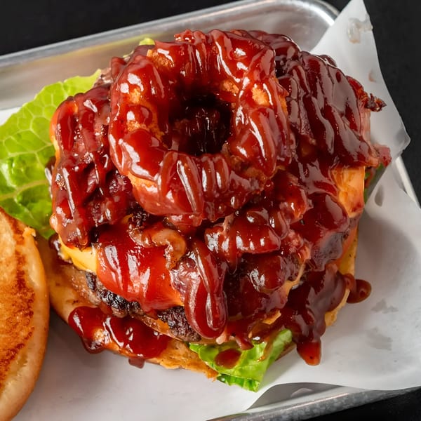 The Burger Life's BBQ burger with onion rings, bacon, cheese, lettuce, and a toasted bun.