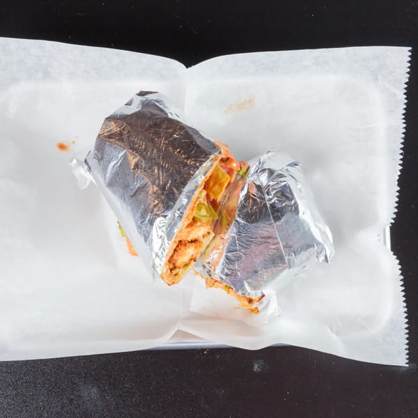 A foil-wrapped The Burger Life chicken sandwich, cut in half, on white paper.