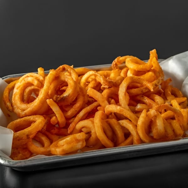 A metal tray filled with golden-brown, seasoned curly fries, lined with white paper.