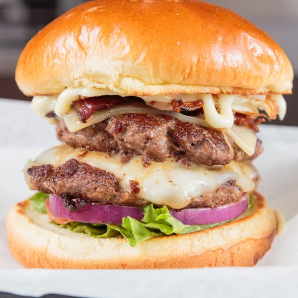 A double patty burger from The Burger Life, with melted cheese, bacon, lettuce, and red onion.