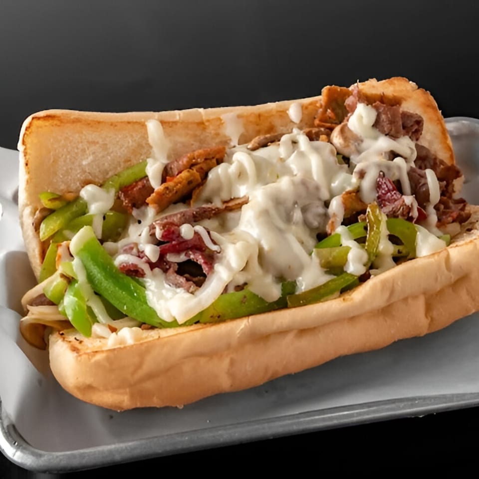 A Philly cheesesteak sandwich with steak, green peppers, onions, and melted cheese on a hoagie roll.