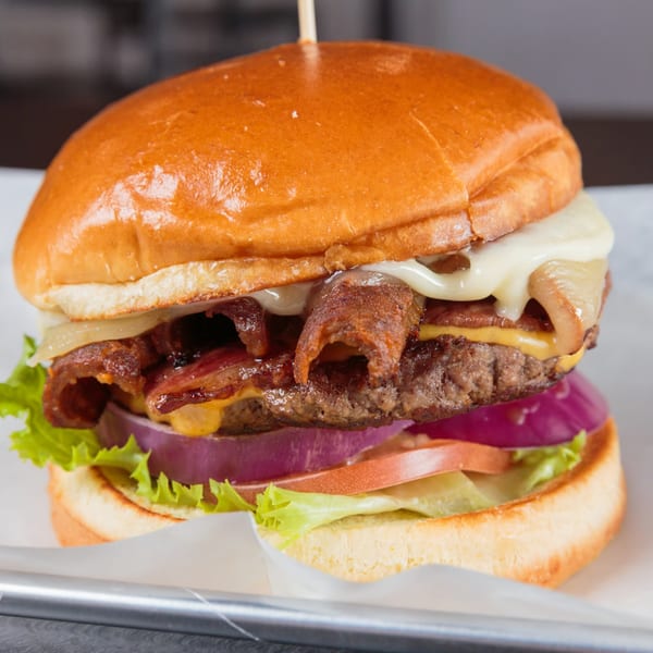 A close-up of a Burger Life burger with bacon, melted cheese, red onion, tomato, and lettuce.